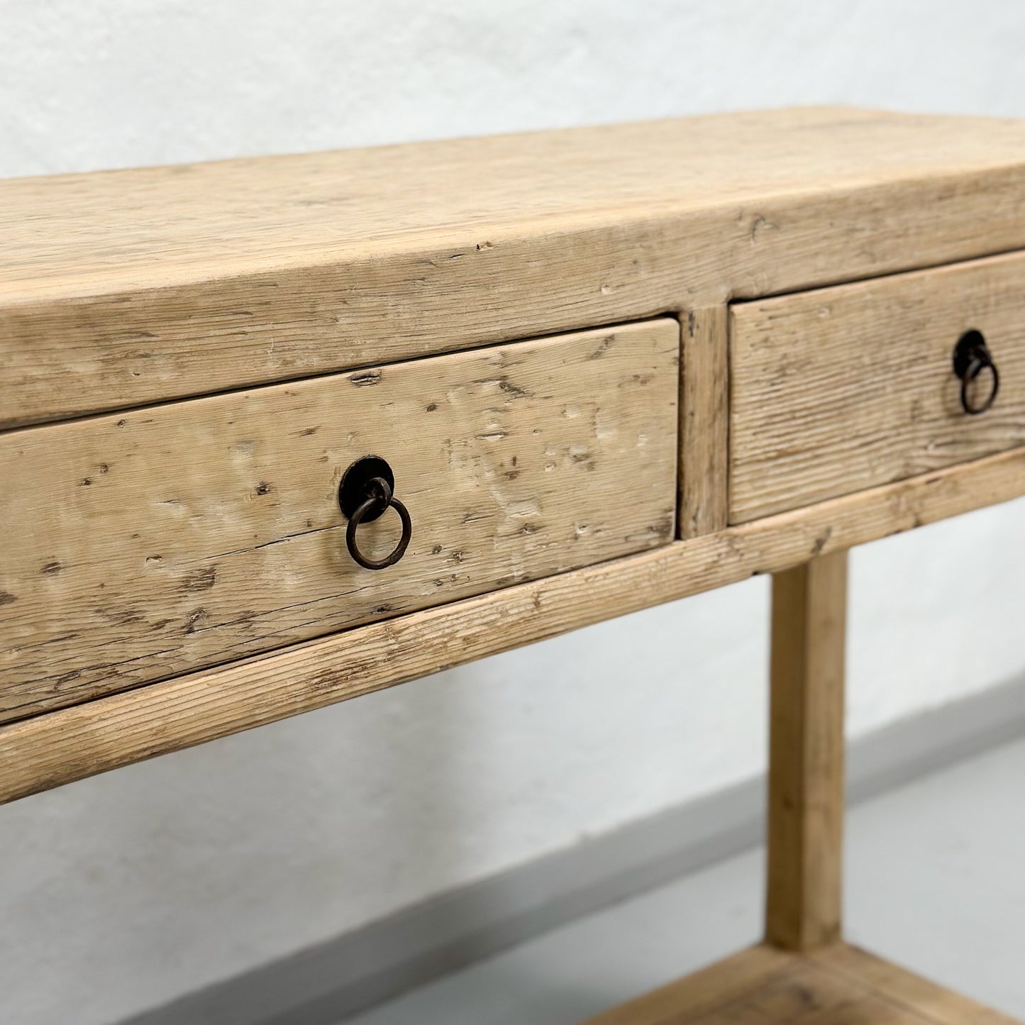 A brown elm wood console table with two drawers and a lower shelf, placed against a plain wall on a white floor.