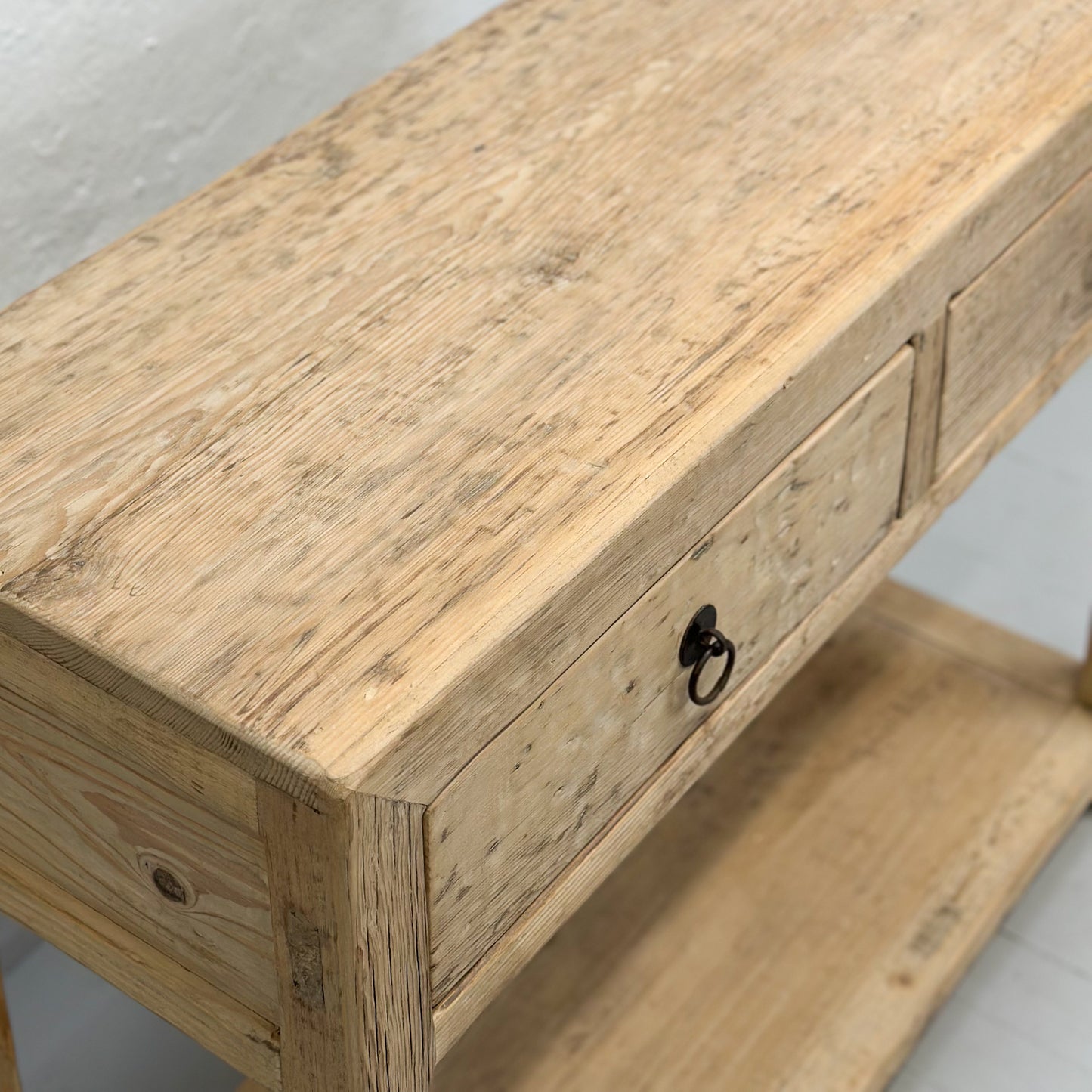 A brown elm wood console table with two drawers and a lower shelf, placed against a plain wall on a white floor.