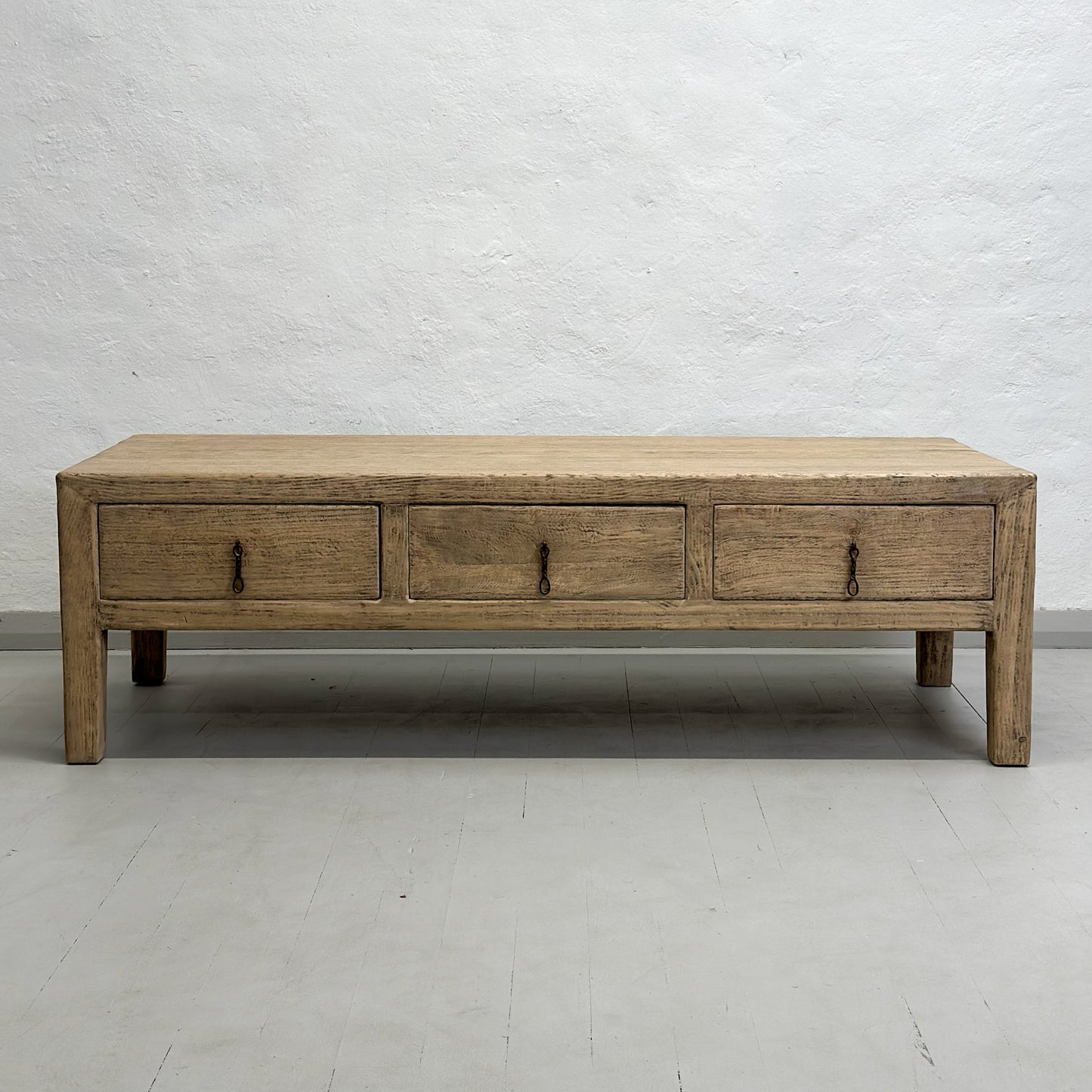 A rustic elm coffee table with three drawers, positioned against a plain background.