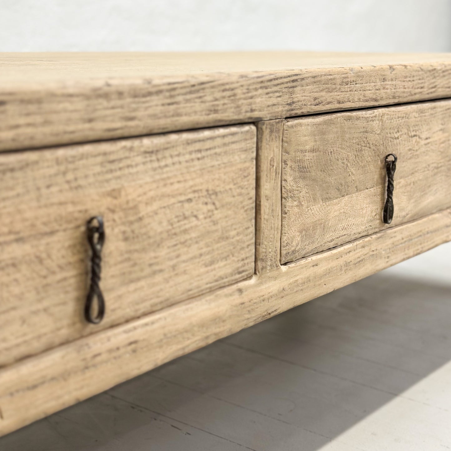 A rustic elm coffee table with three drawers, positioned against a plain background.