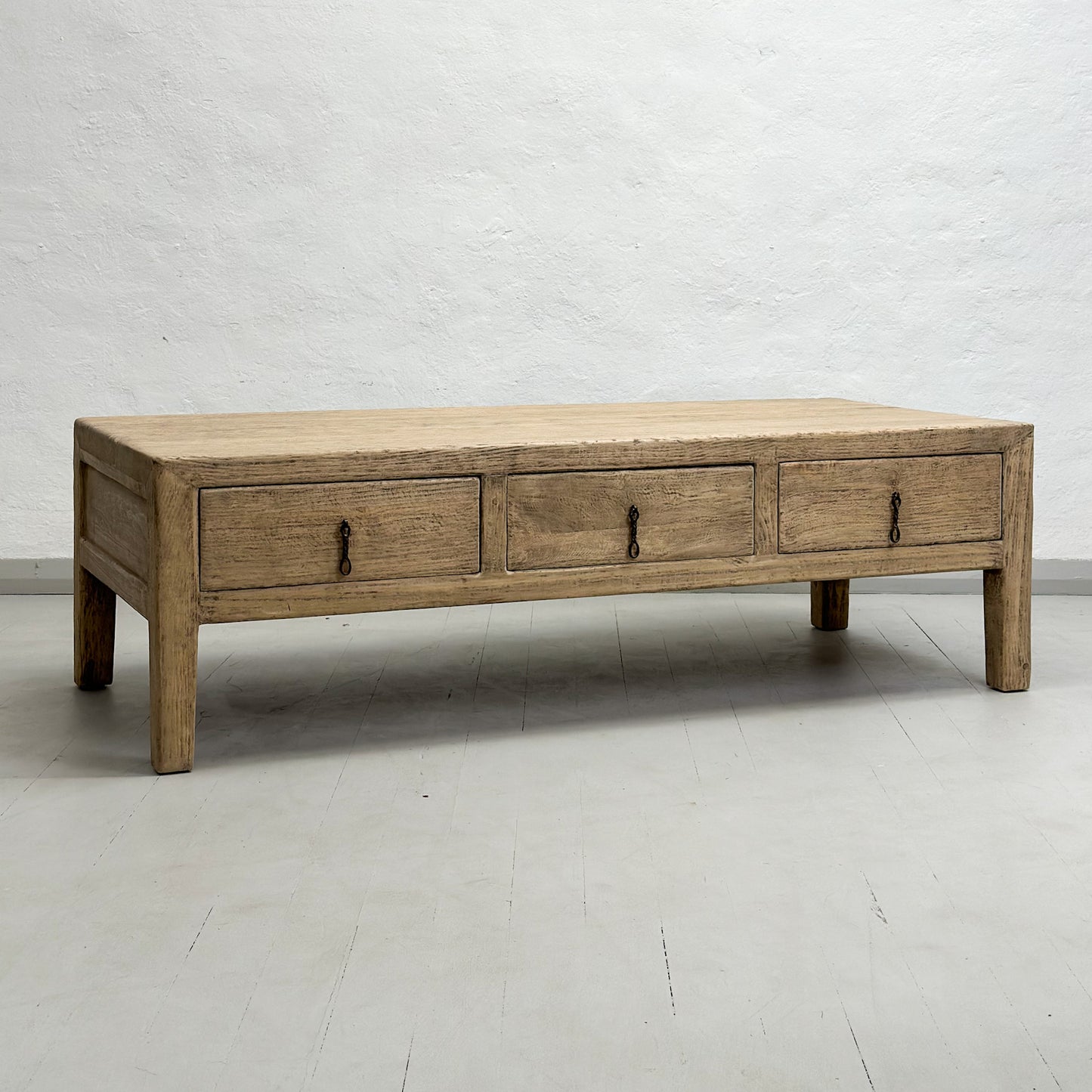 A rustic elm coffee table with three drawers, positioned against a plain background.
