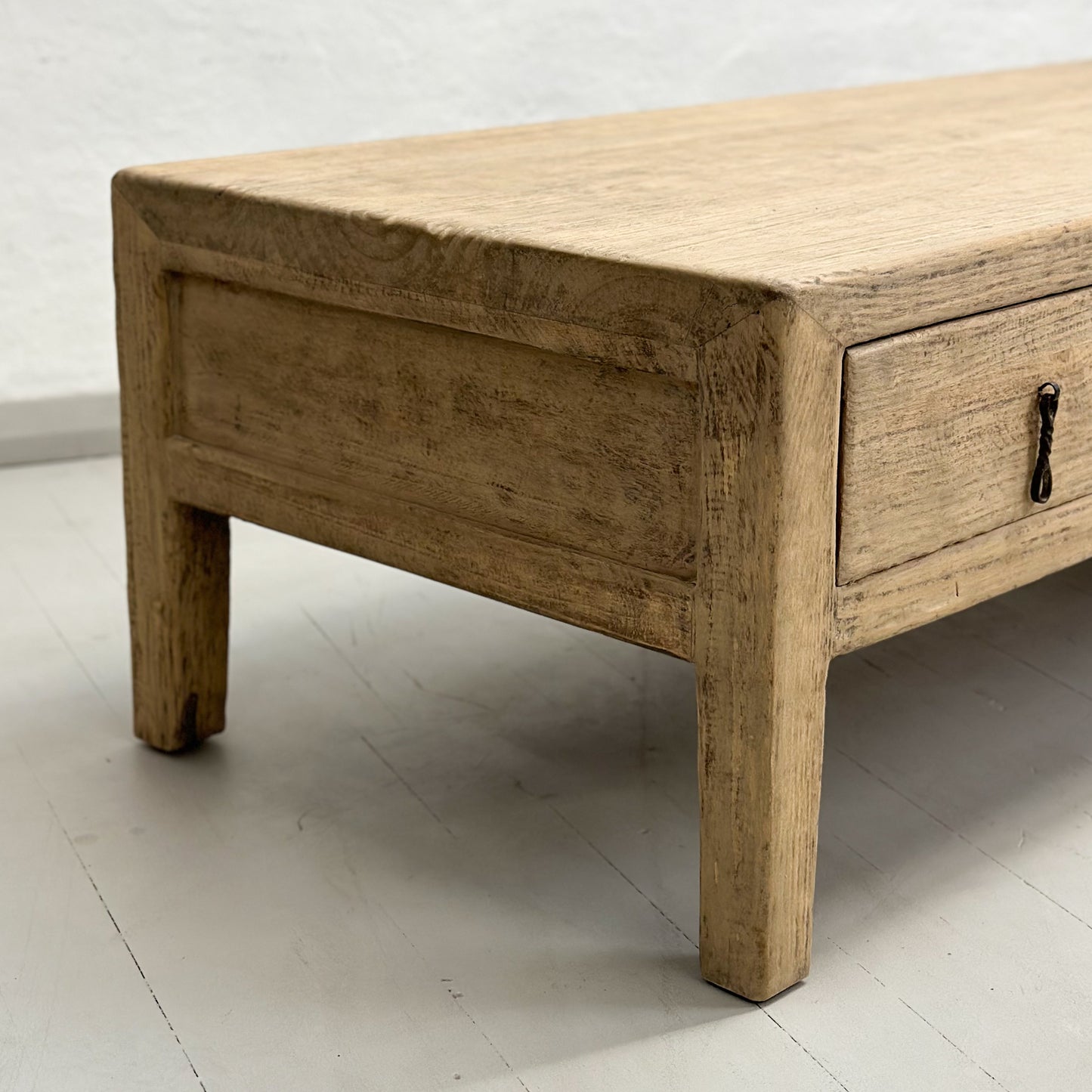 A rustic elm coffee table with three drawers, positioned against a plain background.