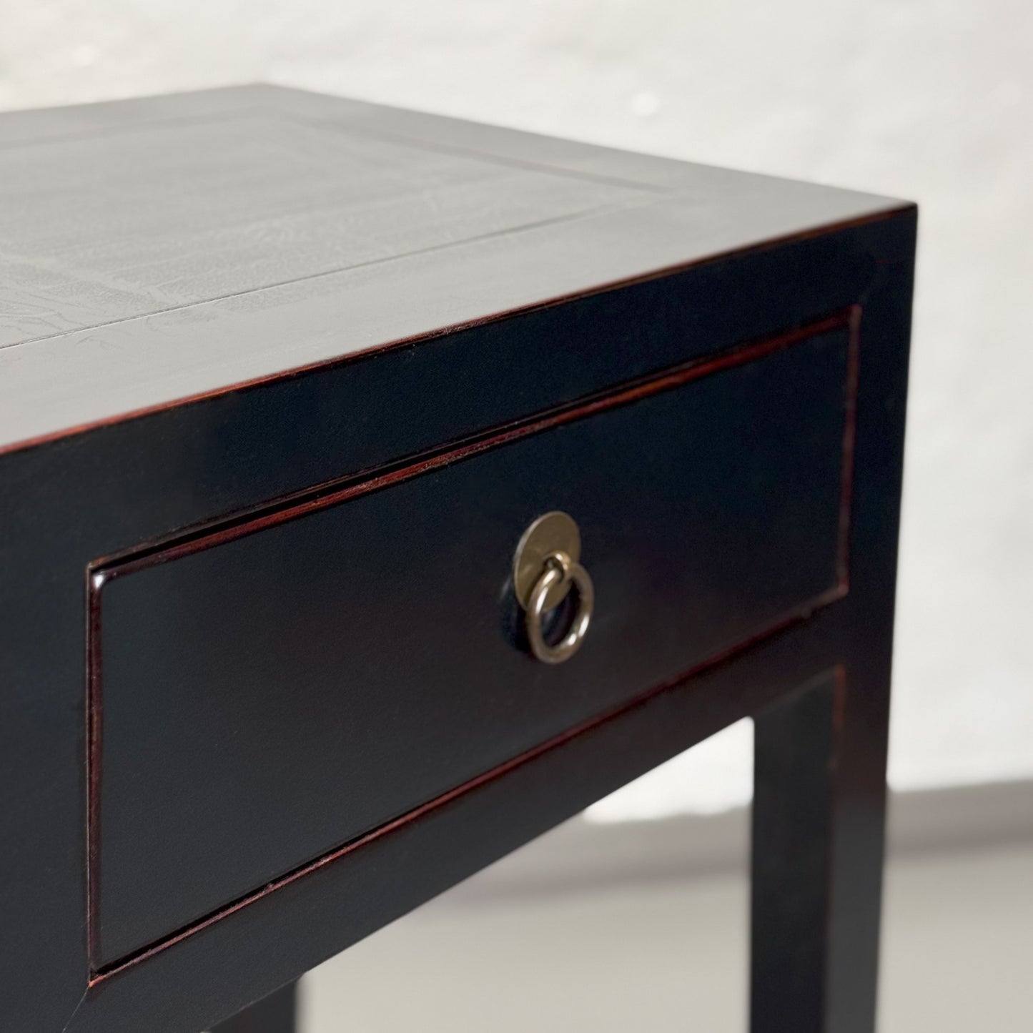 A black wooden console table with four drawers and hoofed legs, placed against a plain wall on a grey floor.