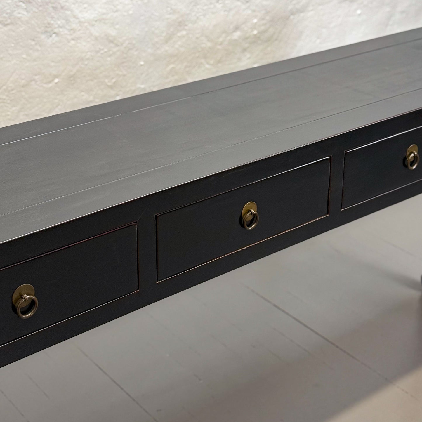 A black wooden console table with four drawers and hoofed legs, placed against a plain wall on a grey floor.