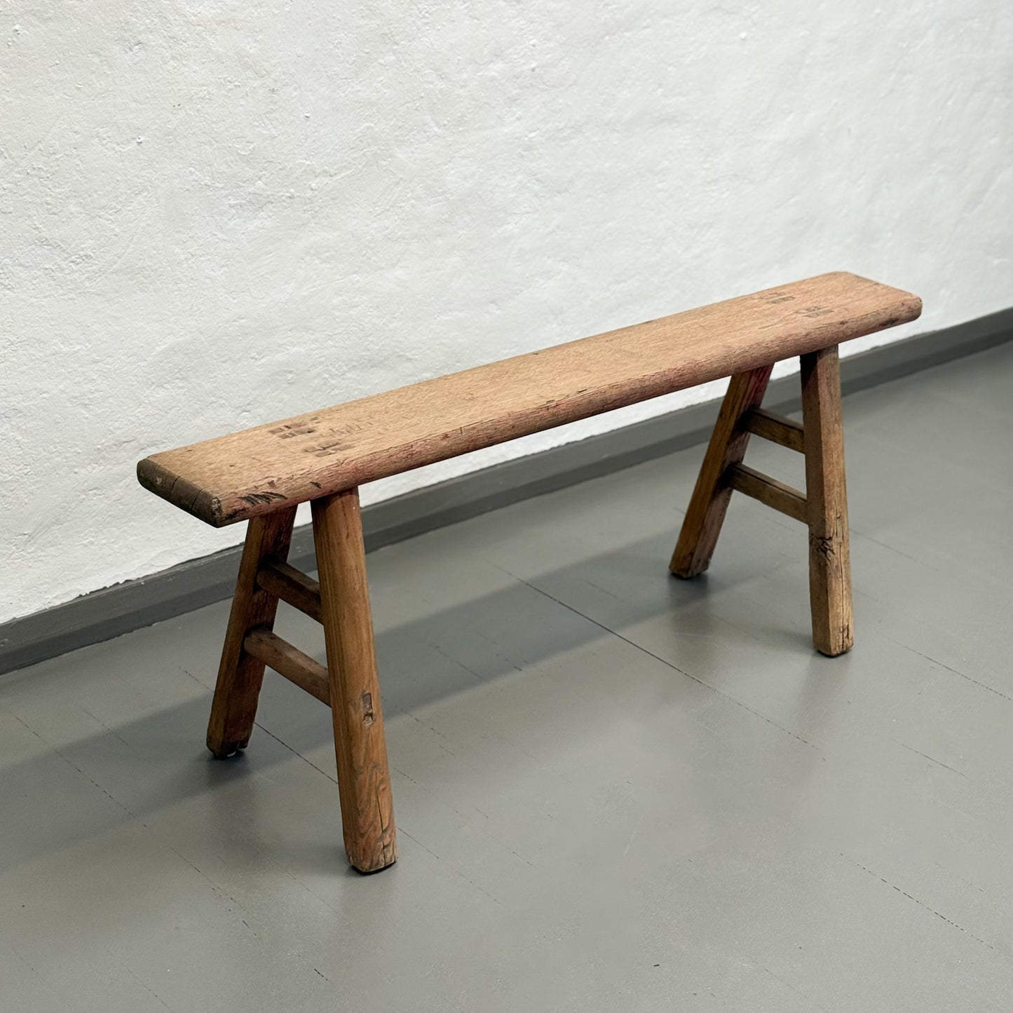 Wooden bench against a white textured wall on a gray floor