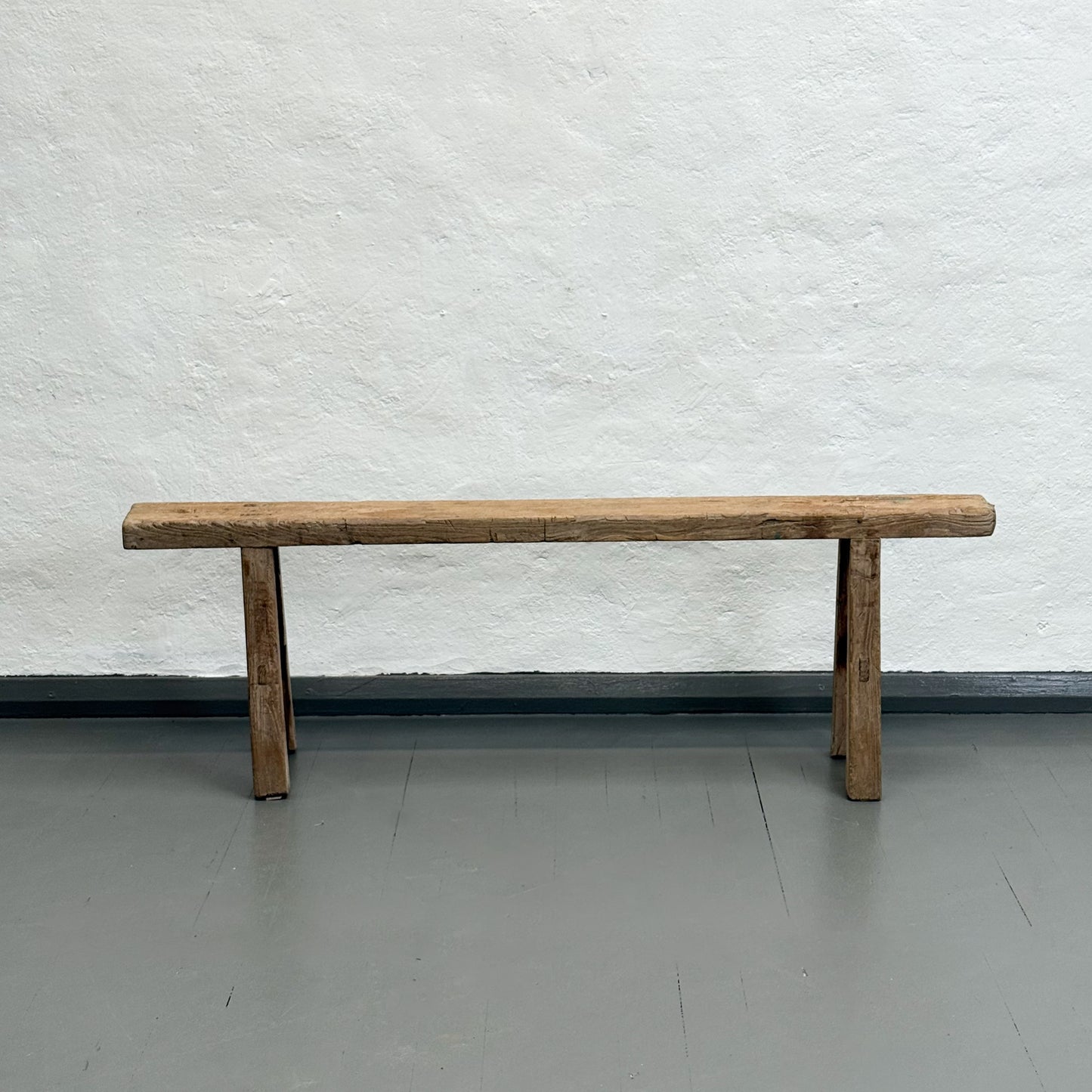 Wooden bench against a textured white wall on a gray floor