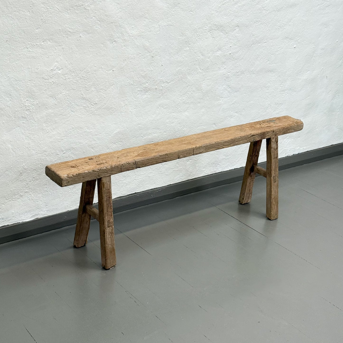 Wooden bench against a textured white wall on a gray floor