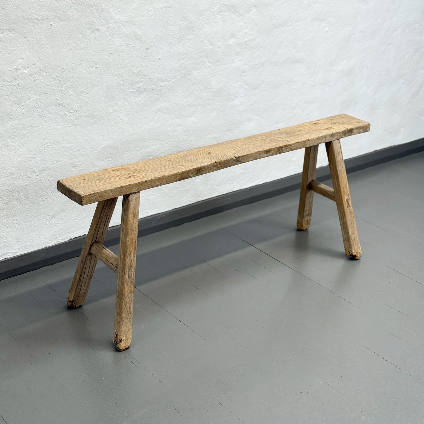 Wooden bench against a white textured wall on a gray floor