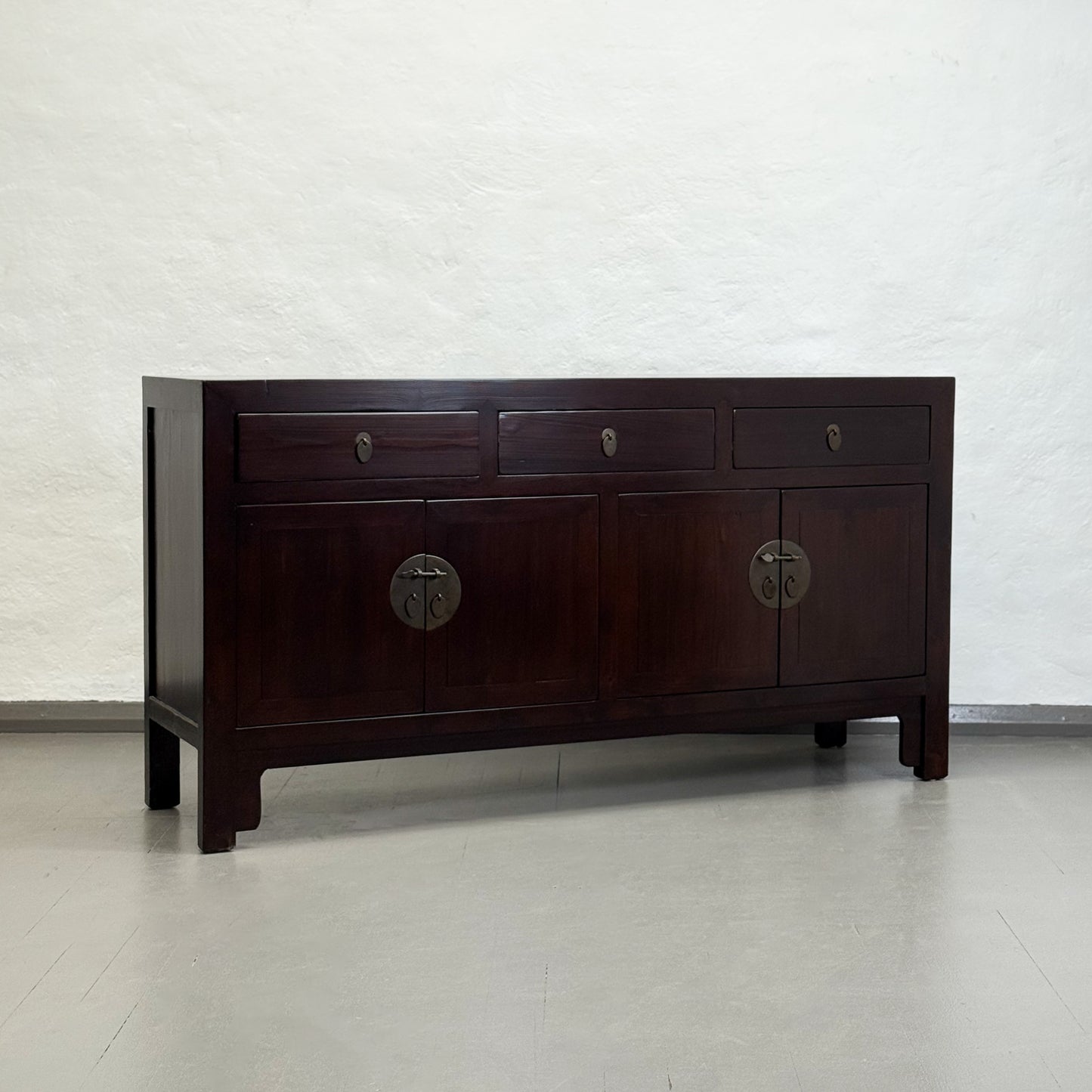 Dark wooden dresser with multiple drawers and circular handles on a plain background