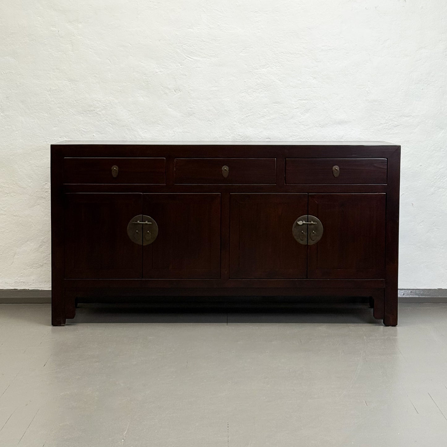 Dark wooden dresser with circular handles on a light gray floor and white wall background