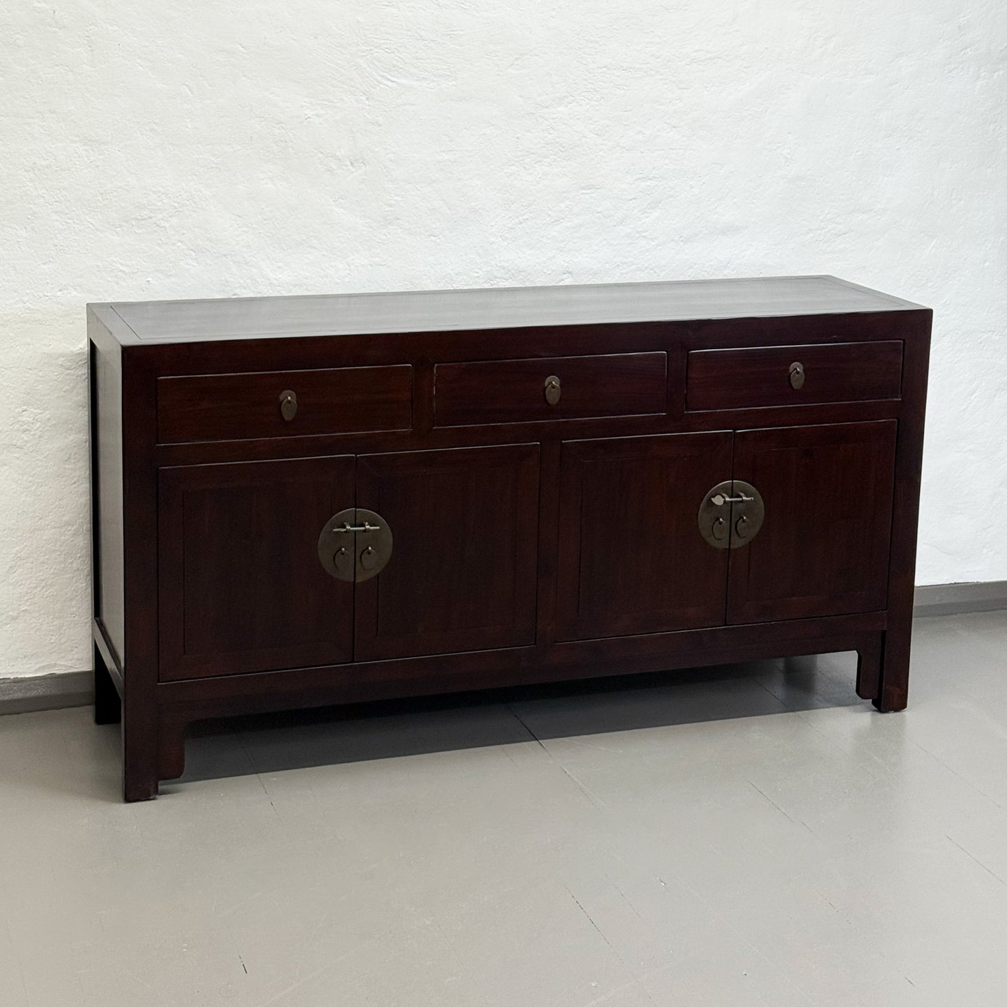 Dark wooden sideboard with circular handles against a light brick wall.