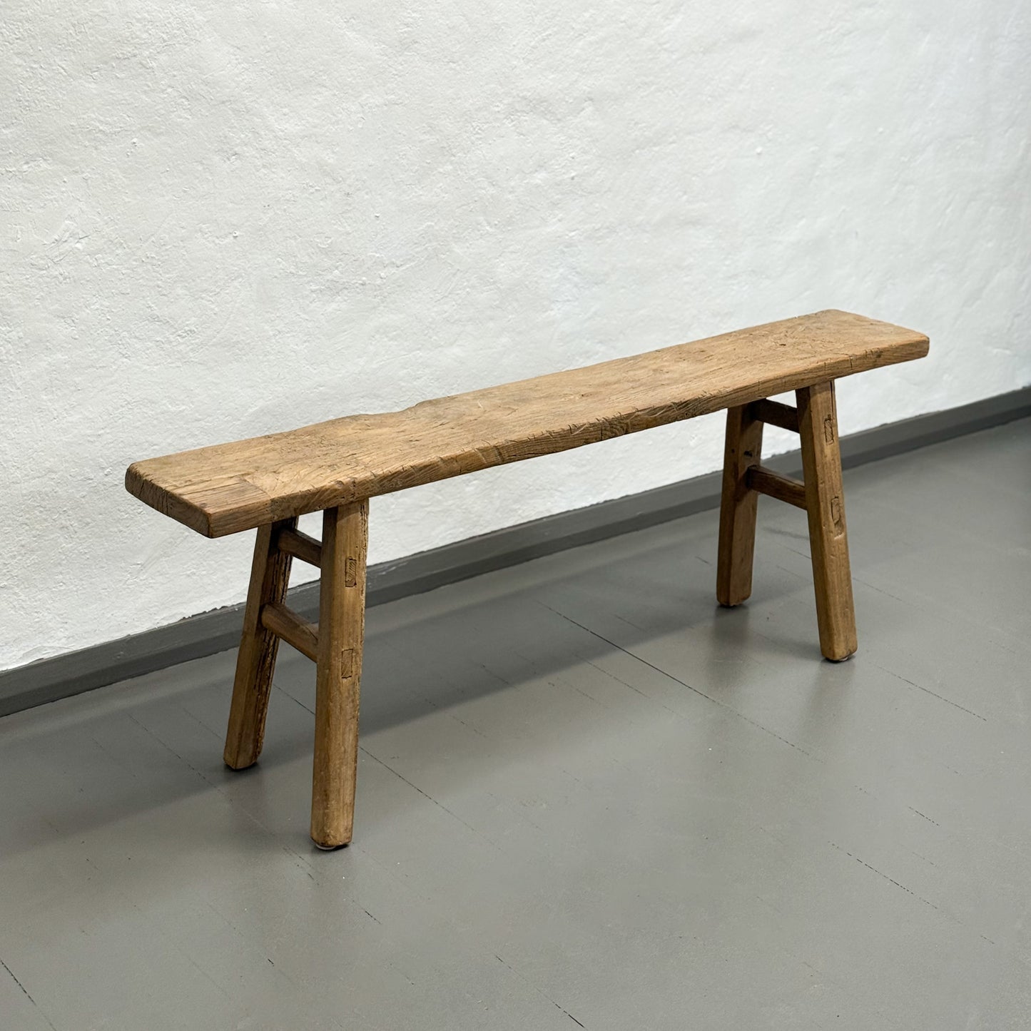 Wooden bench against a textured white wall on a gray floor