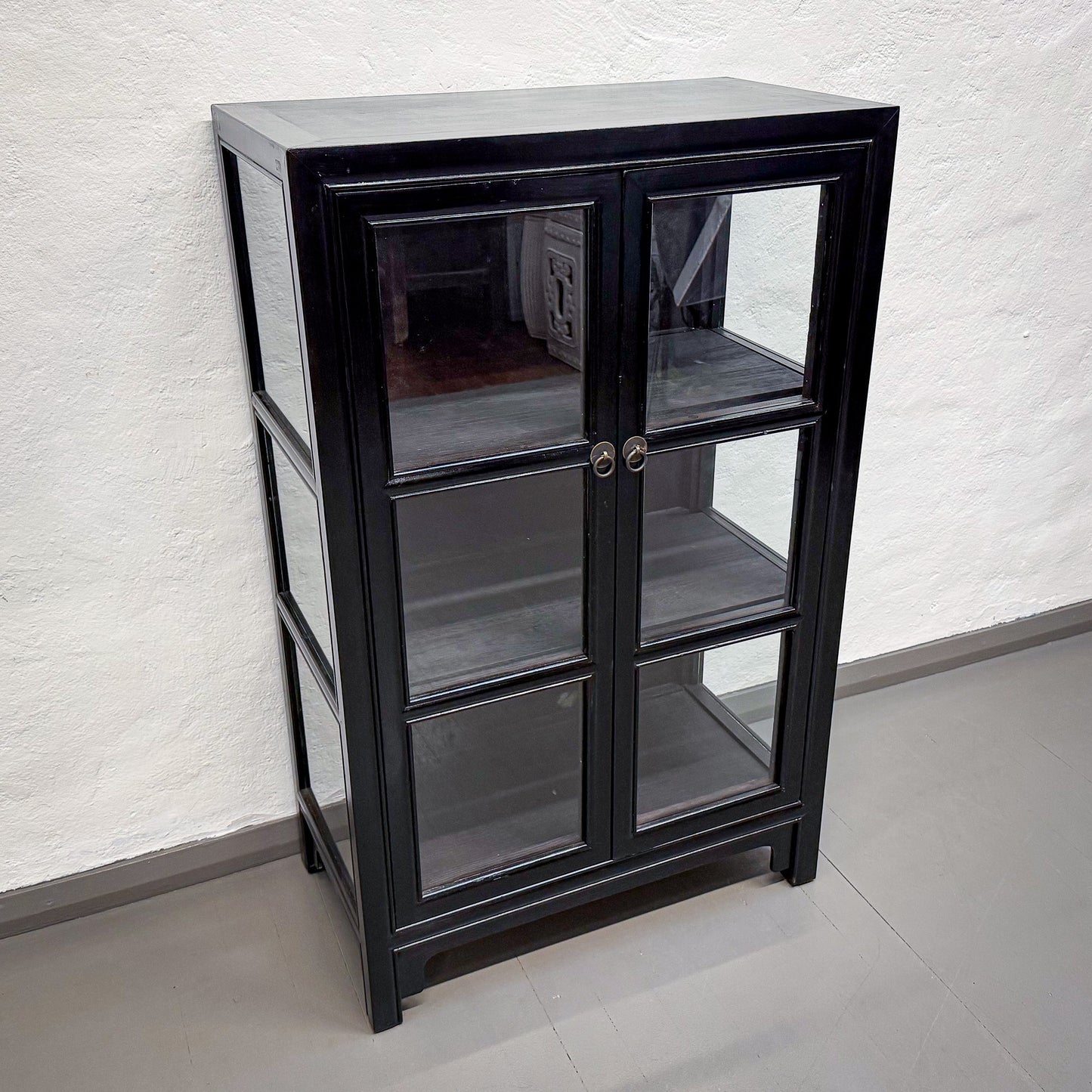 Black glass-fronted cabinet against a white textured wall.