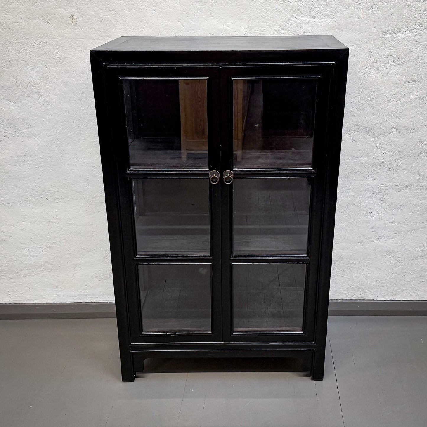 Black glass-fronted cabinet against a white brick wall.