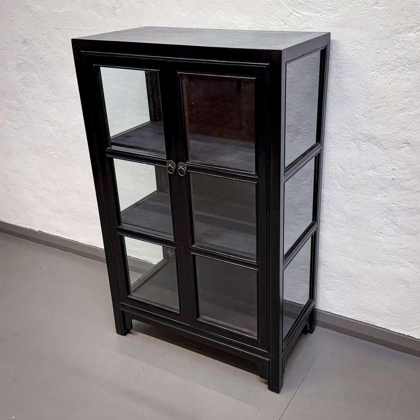 Black glass-fronted cabinet against a white textured wall.