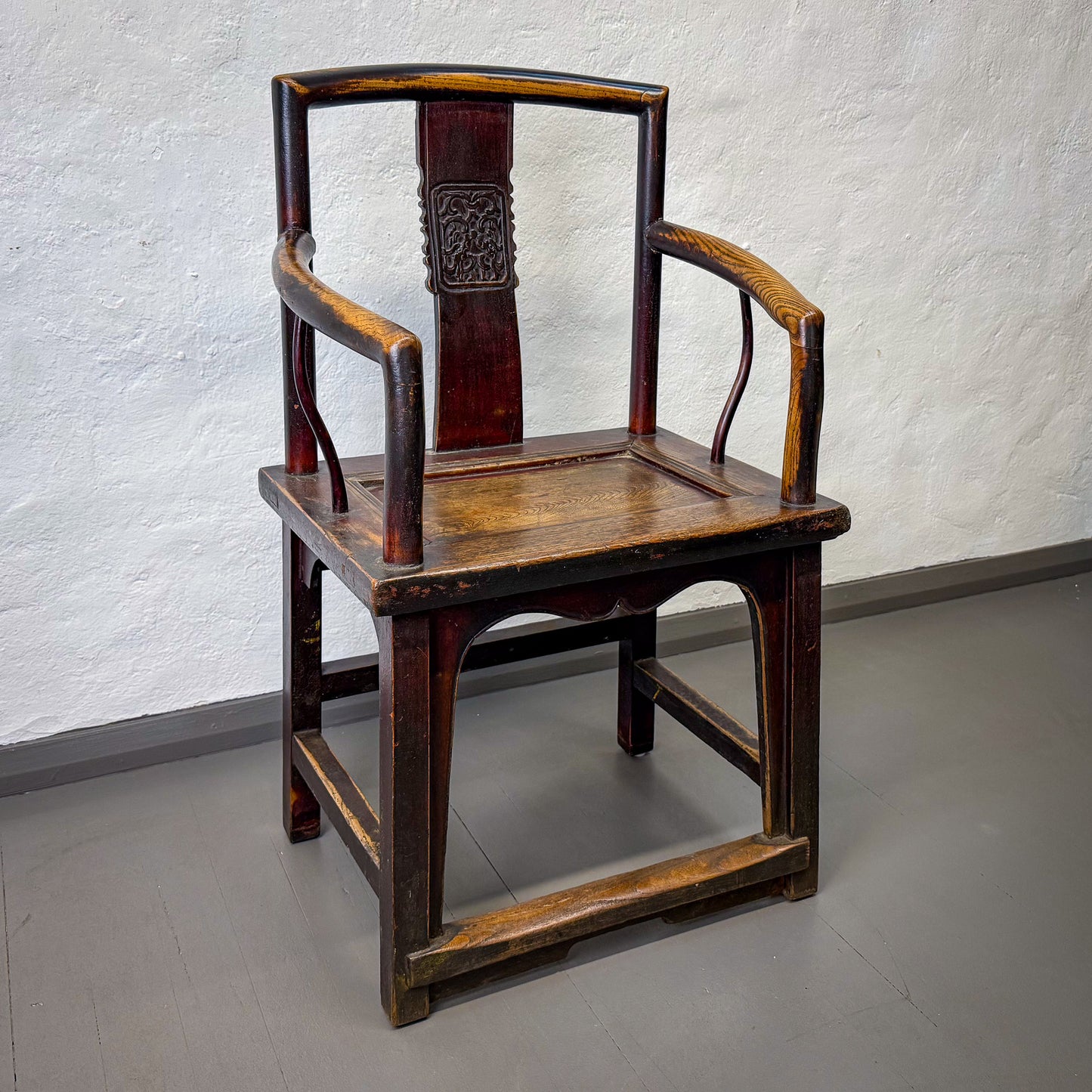 Traditional wooden chair with intricate design against a plain wall.