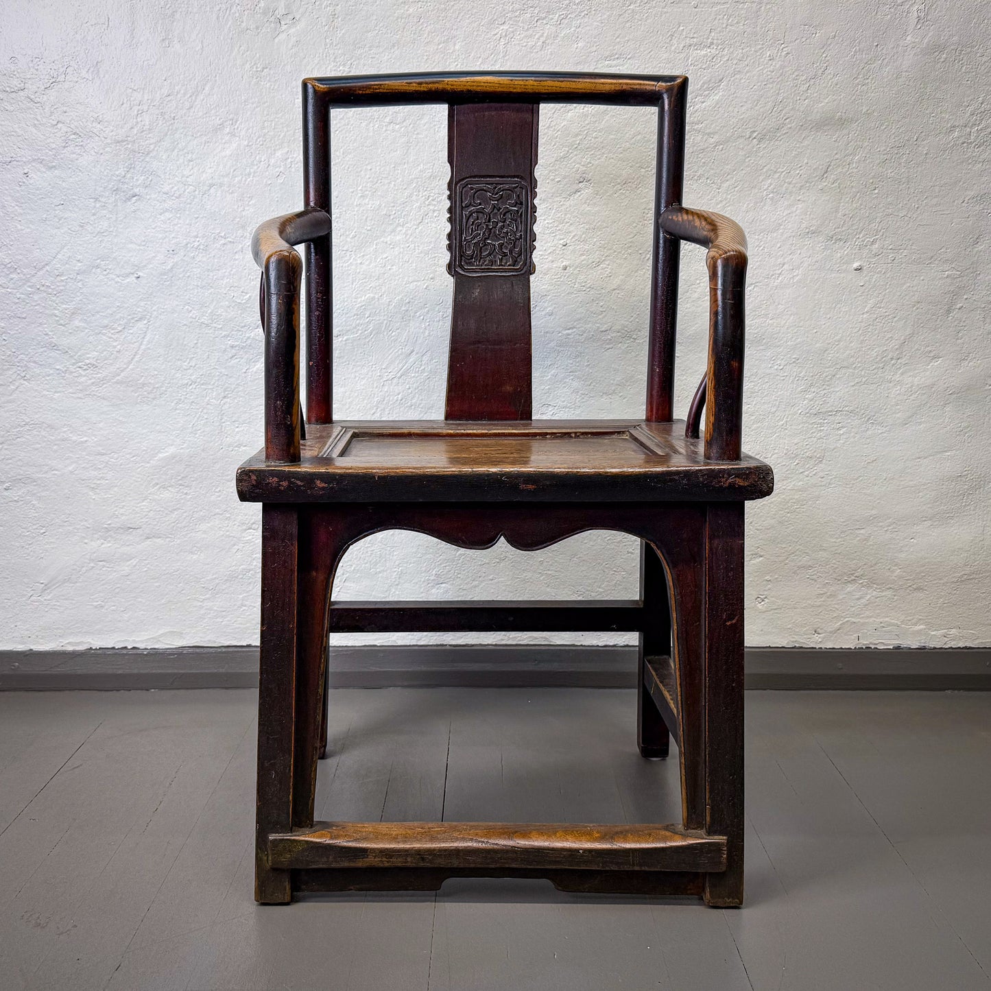 Traditional wooden chair with intricate backrest against a plain wall.