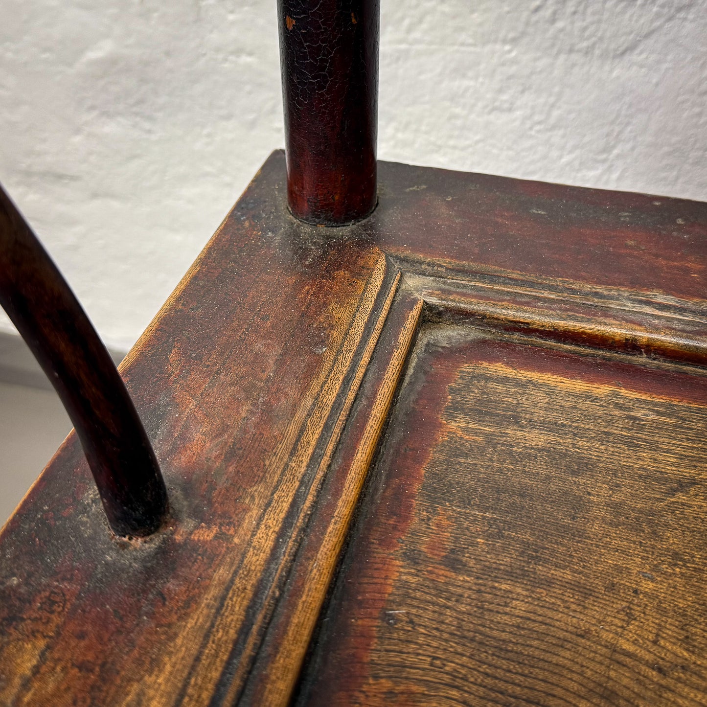 Close-up of a wooden chair with a worn finish against a white wall.