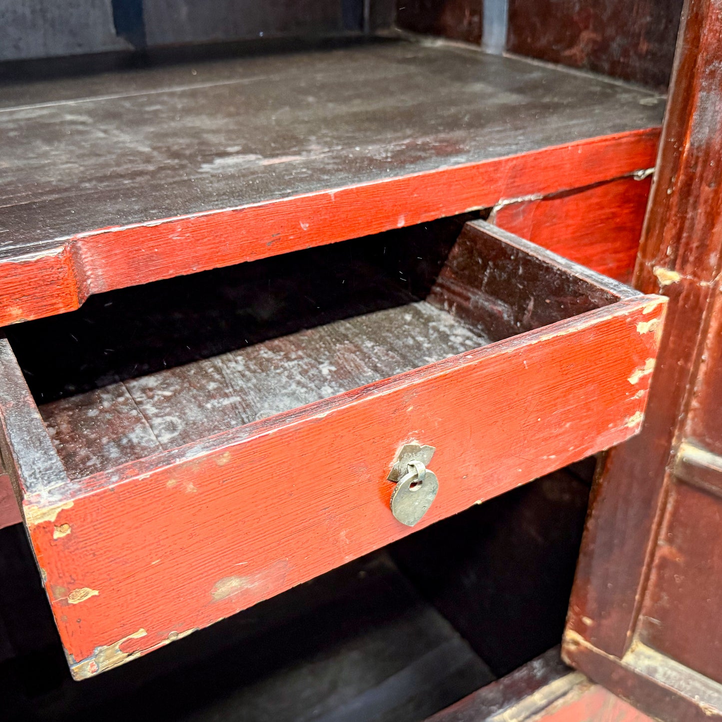 Red wooden drawer with a metal handle on an old wooden cabinet.