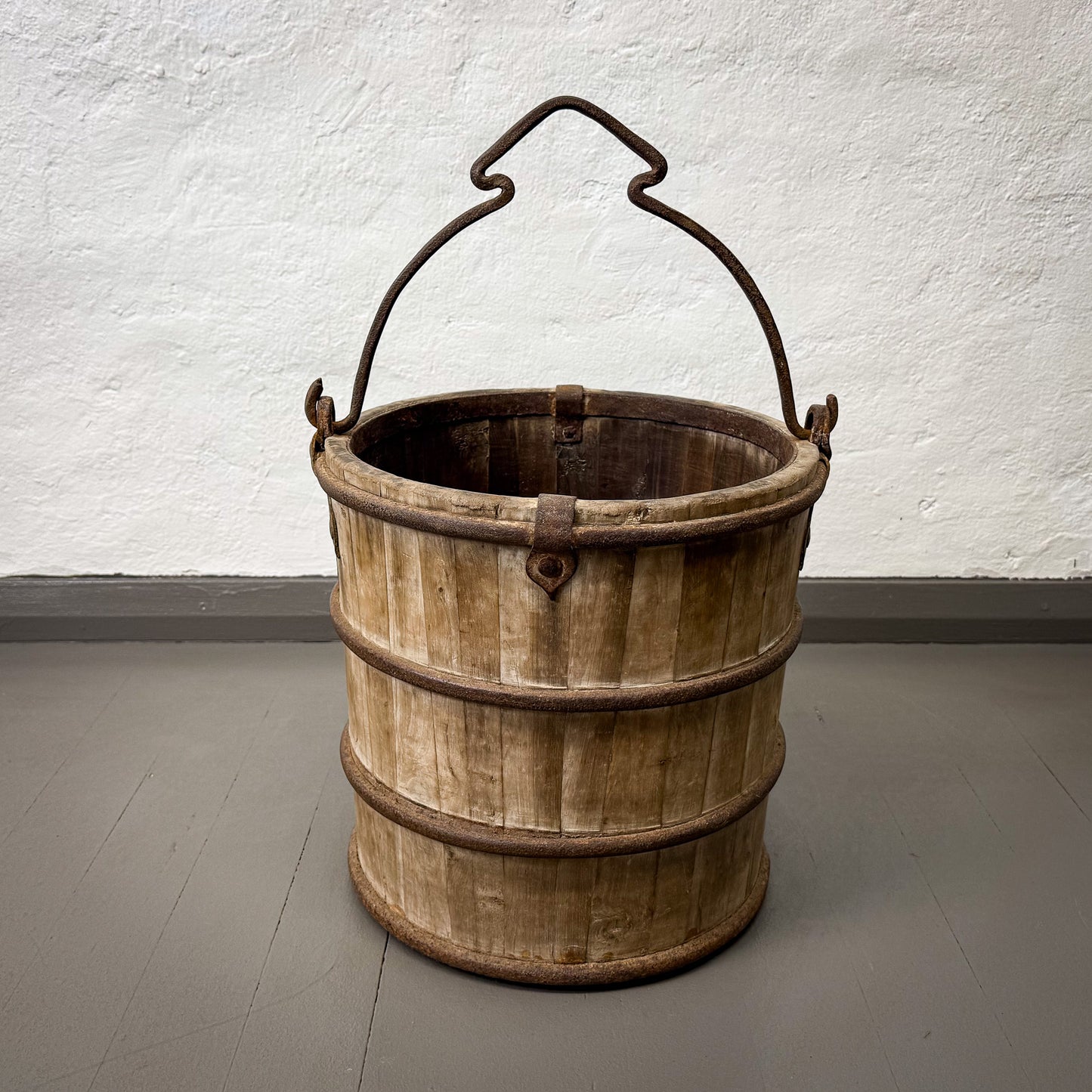 Wooden bucket with metal handle on a gray floor against a white wall