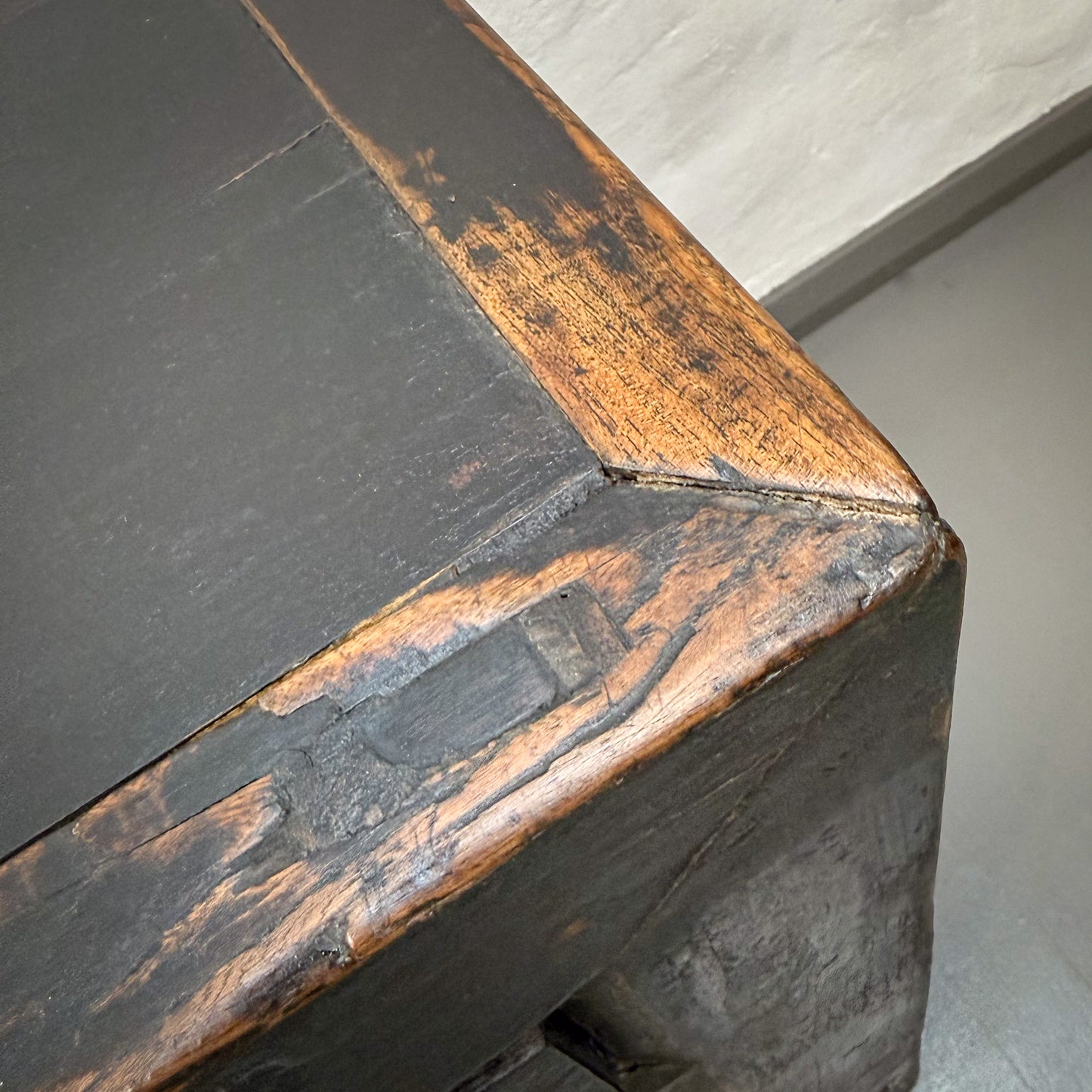 Close-up of a wooden surface with dark paint and visible grain, on a plain background.