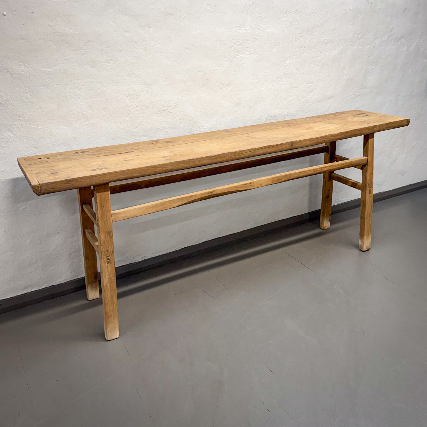 Long wooden bench against a plain wall on a gray floor