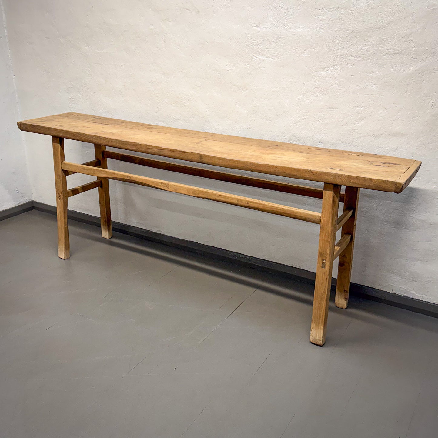 Wooden bench against a plain wall on a gray floor