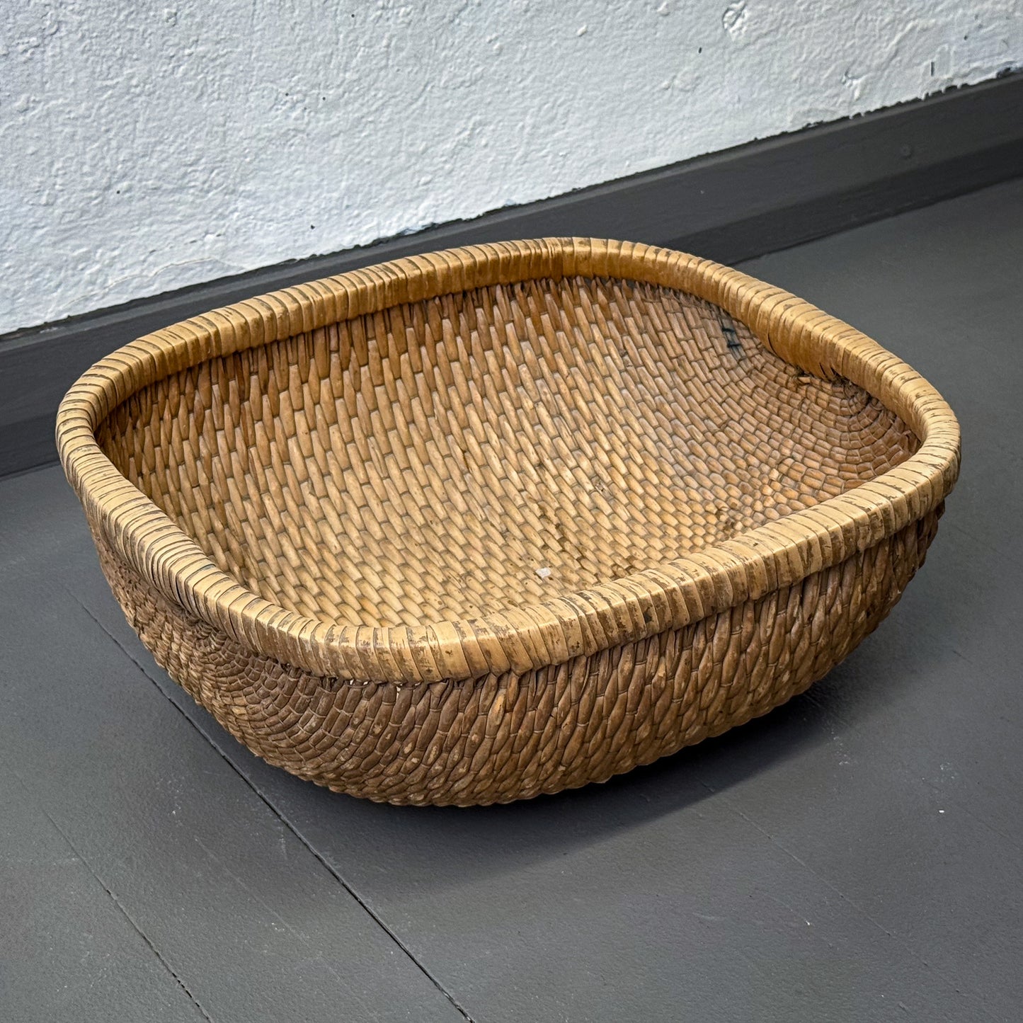Woven basket on a gray floor with a white wall background