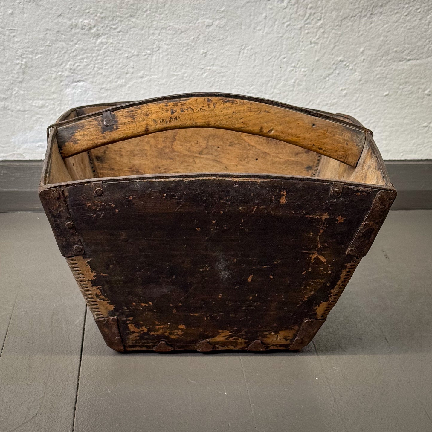 Vintage wooden basket with a dark brown finish on a gray floor.