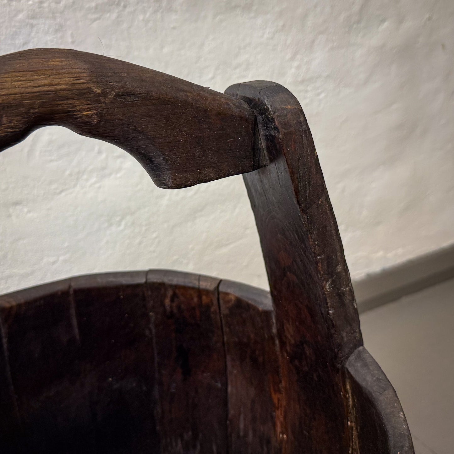 Close-up of an old wooden chair with a worn armrest against a textured white wall.