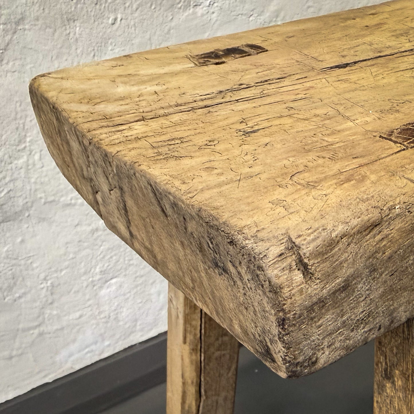 Close-up of a rustic wooden bench against a white wall.
