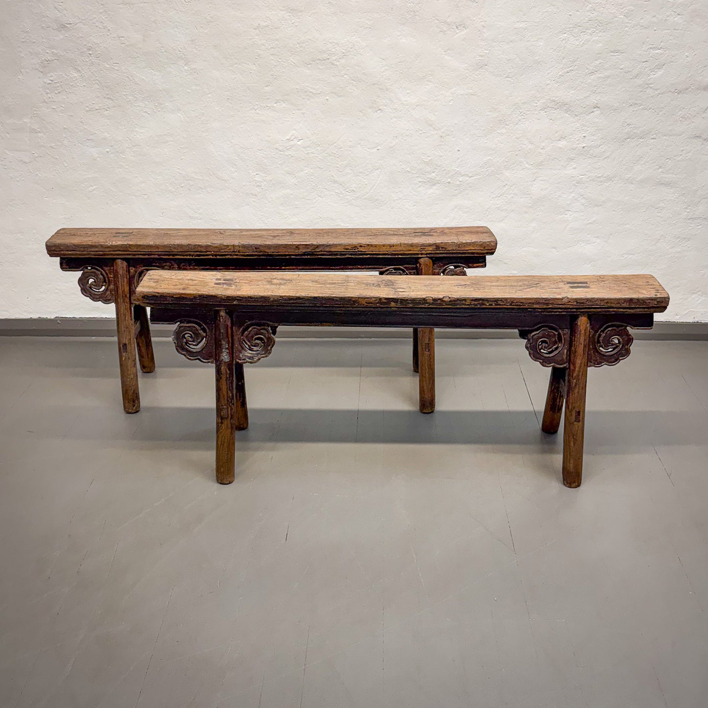 Two wooden benches with decorative carvings on a plain floor and wall.