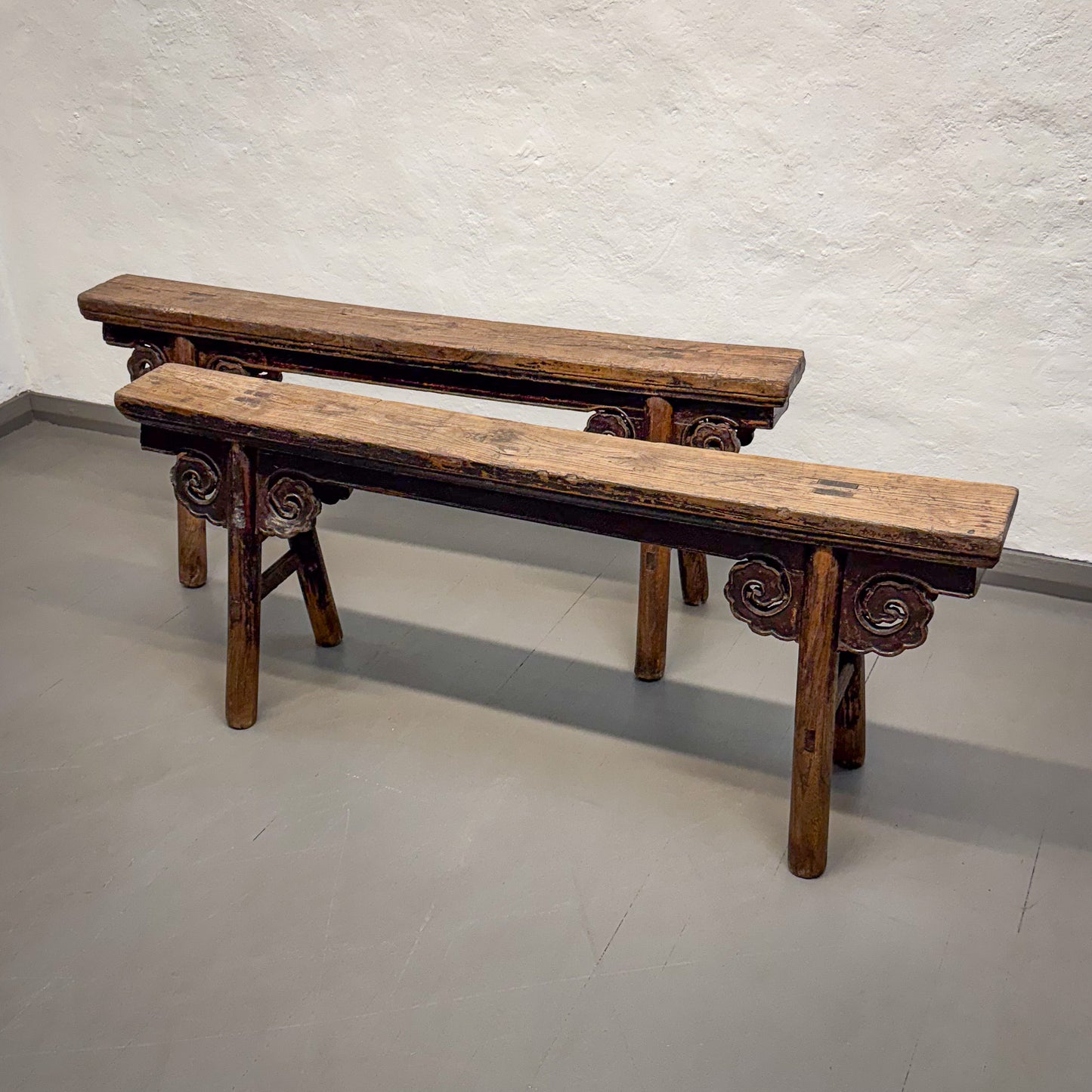 Two wooden benches with decorative carvings on a plain floor and wall background