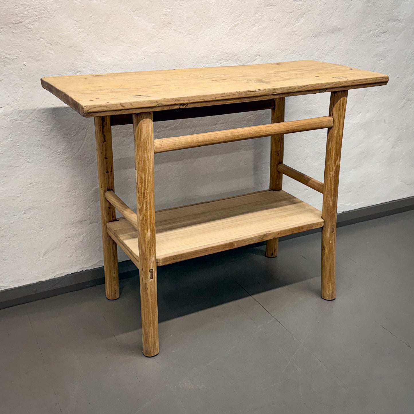 Wooden table with a shelf against a plain wall