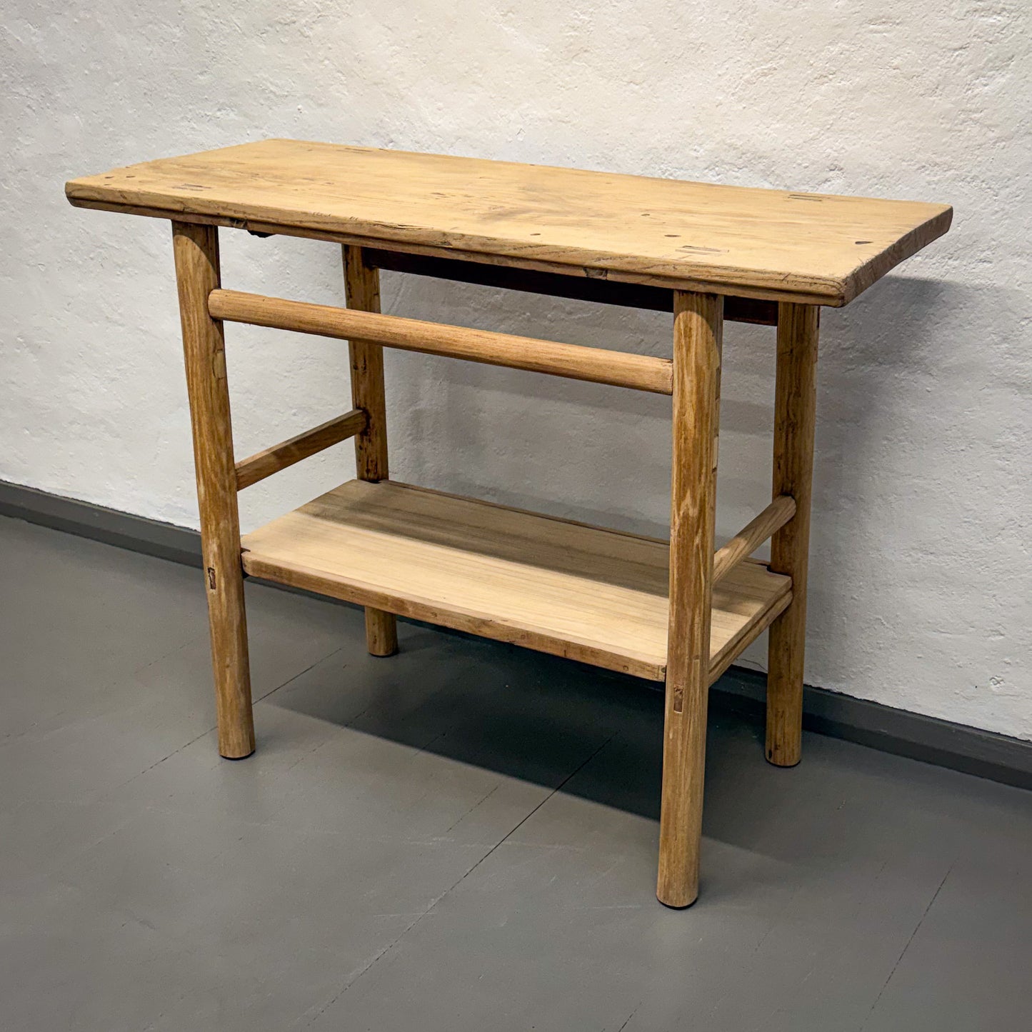 Wooden table with a shelf against a plain wall