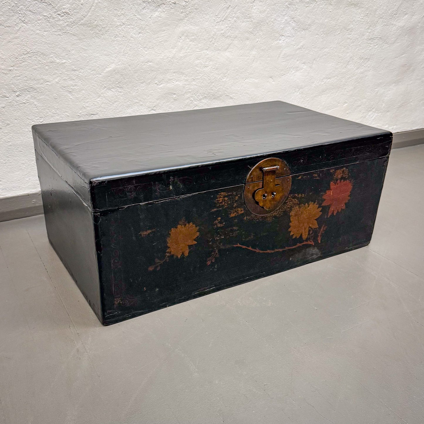Black wooden trunk with floral designs on a light gray floor.