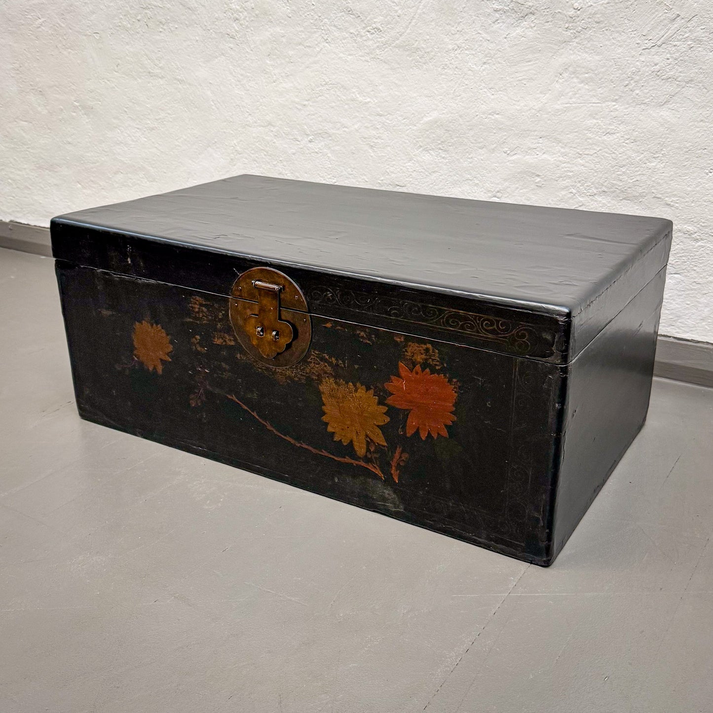 Black metal trunk with floral designs on a textured wall background