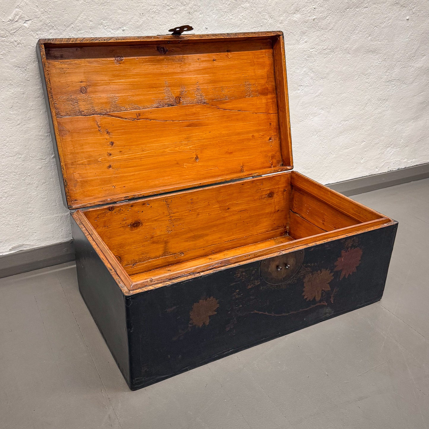 Wooden trunk with black base on a gray floor against a white wall