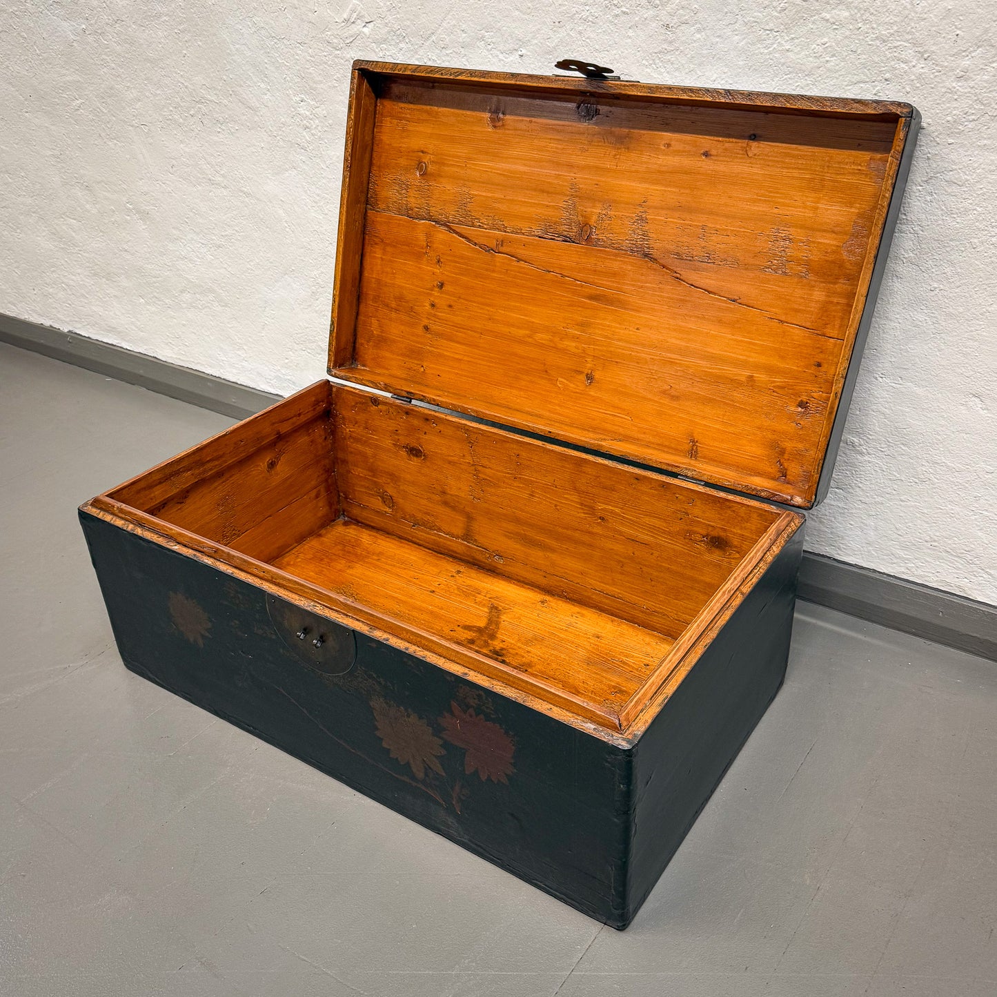 Wooden trunk with black base on a gray floor against a white wall