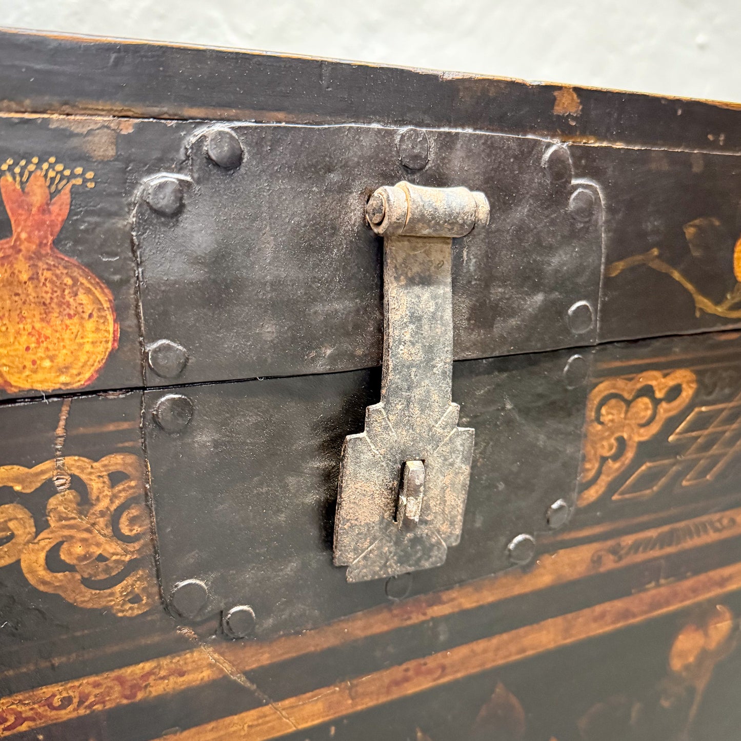 Close-up of a black metal trunk with decorative gold patterns and a lock.
