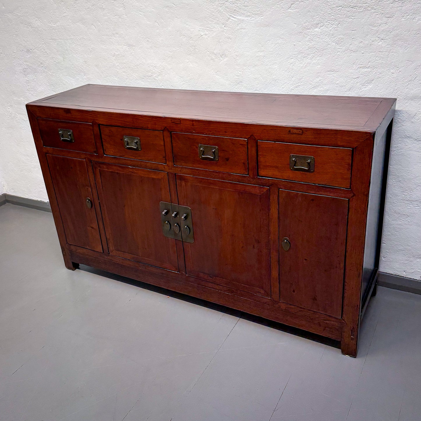 Wooden sideboard with brass handles against a white wall.