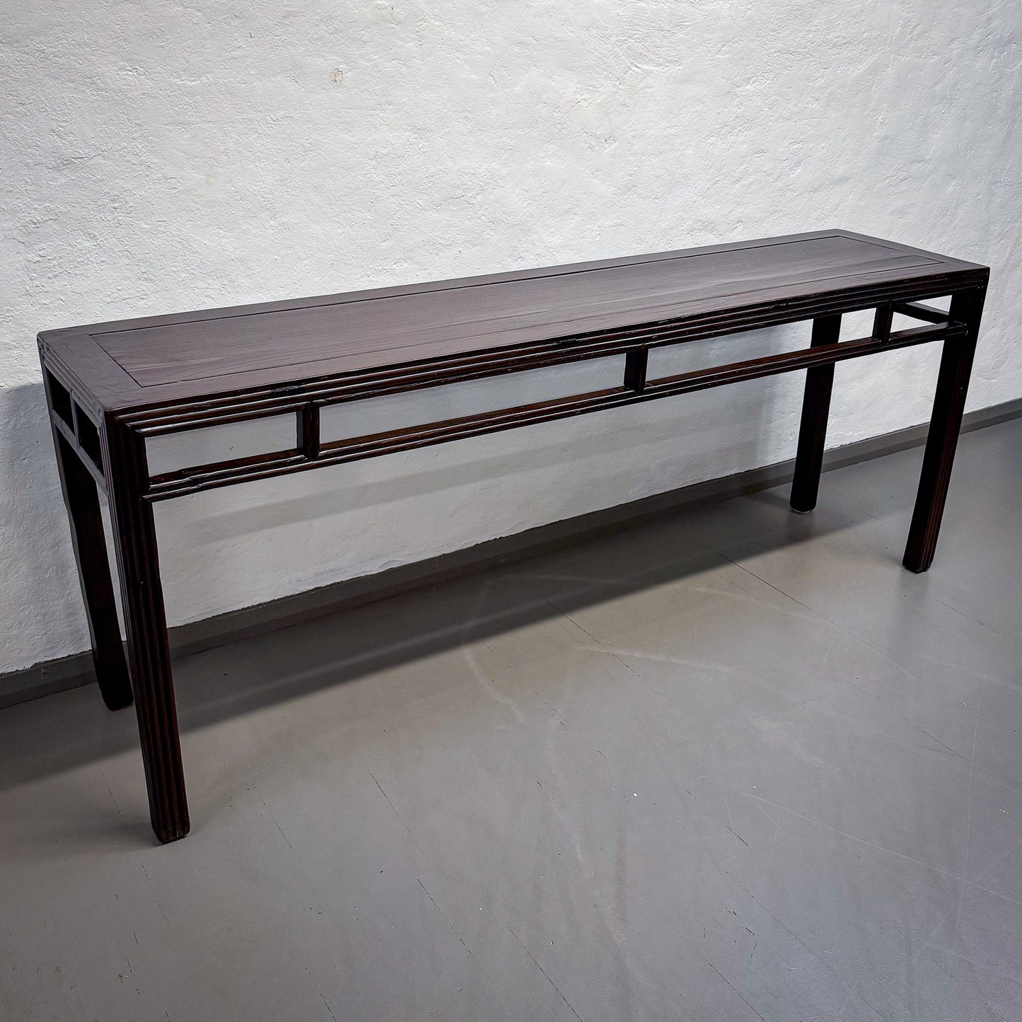 Dark wooden bench against a textured white wall.