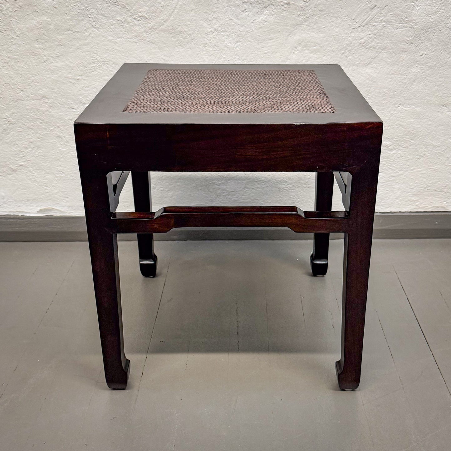 Wooden side table with woven top against a white wall