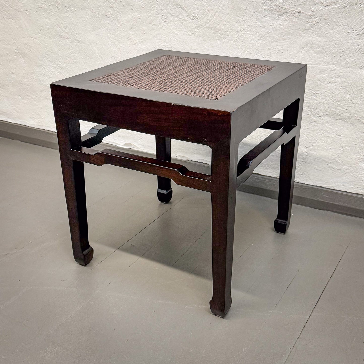 Small wooden stool with woven top on a plain floor and wall background