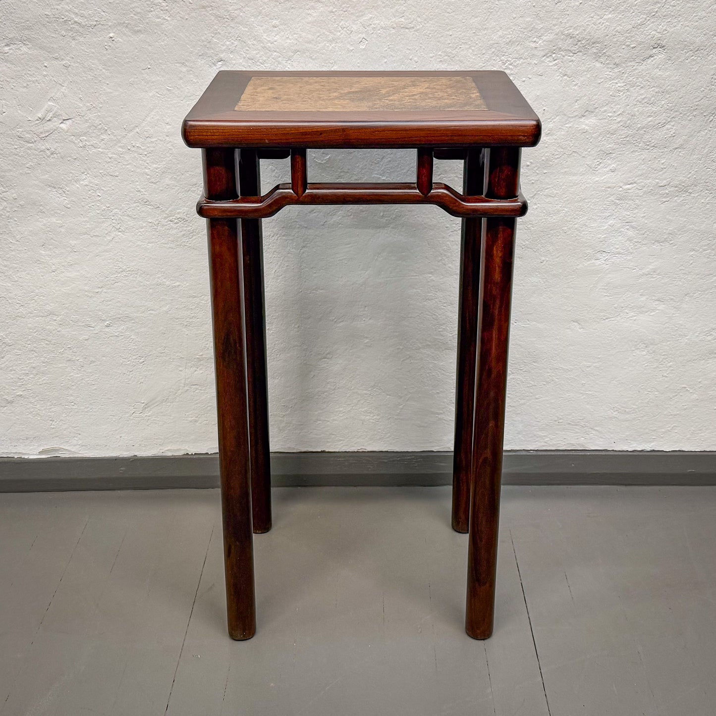 Wooden side table with decorative top against a plain wall