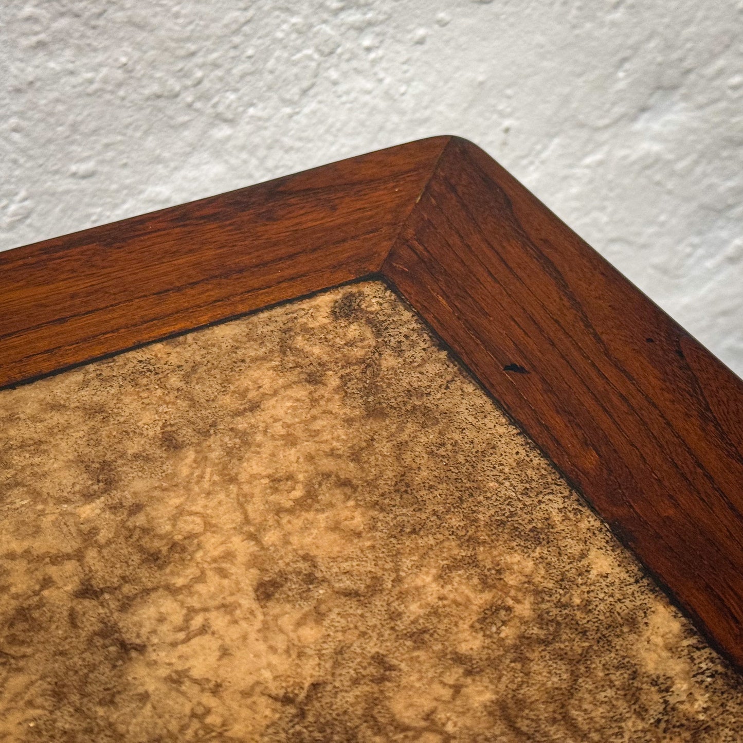 Close-up of a wooden frame corner with a textured brown mat against a white wall.