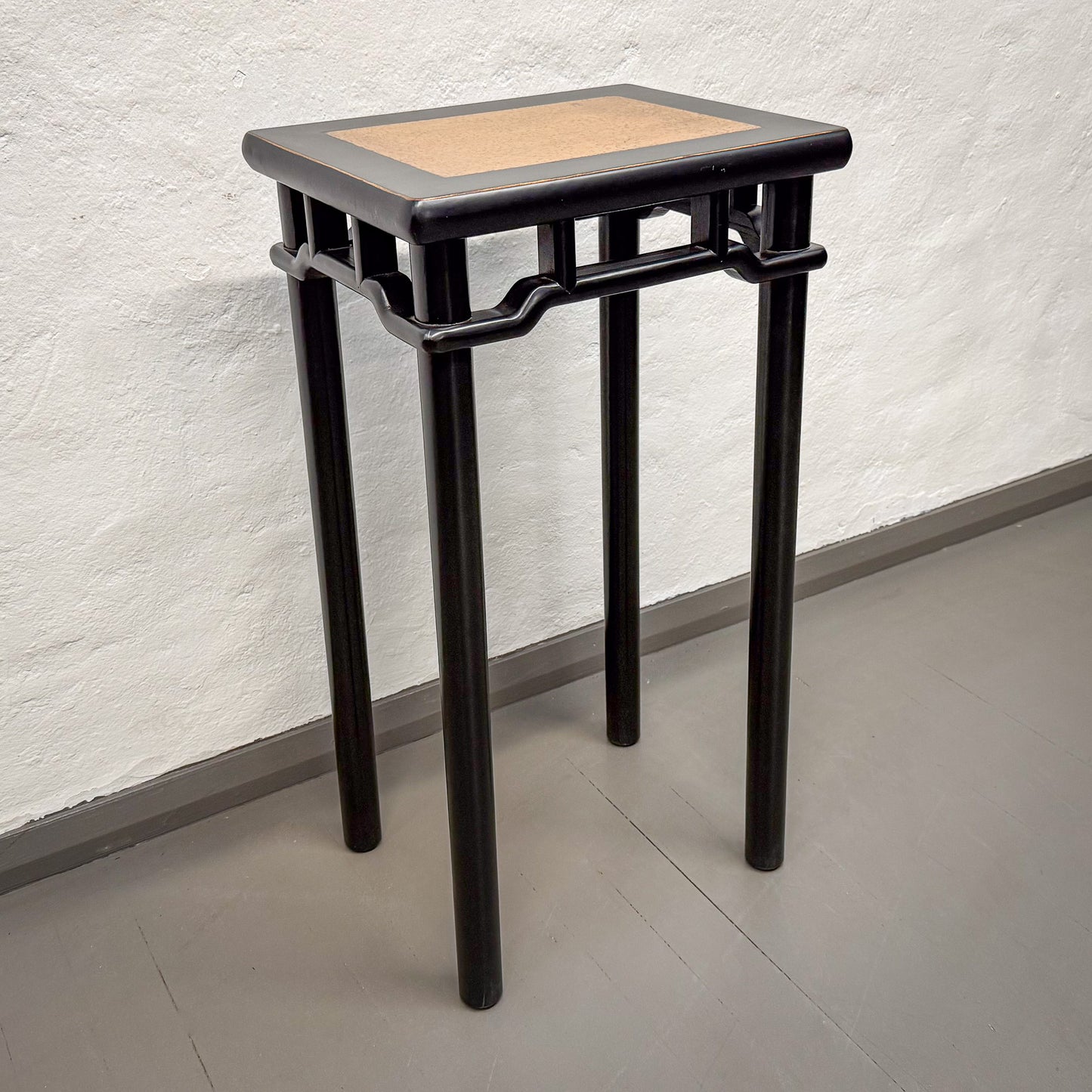 Black wooden side table with a beige top against a white textured wall.