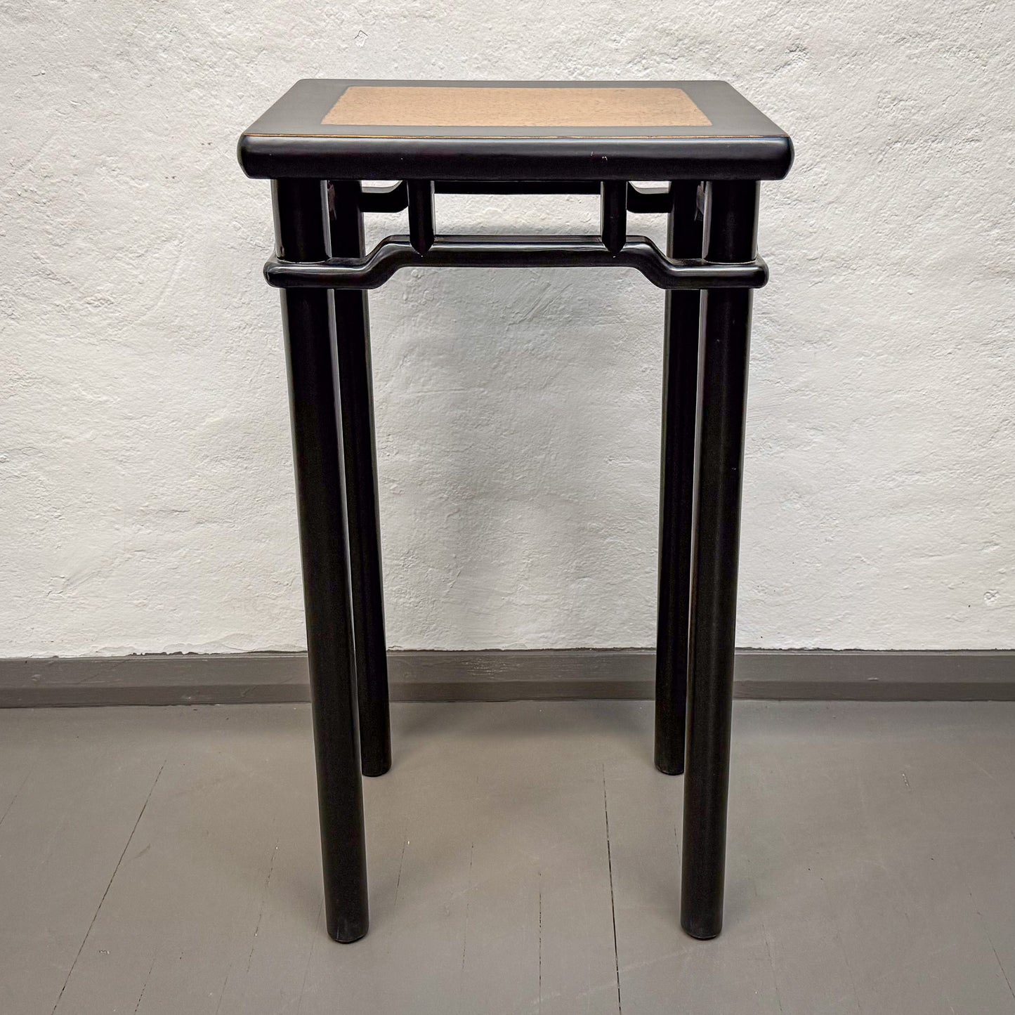 Black side table with a woven top against a white wall.