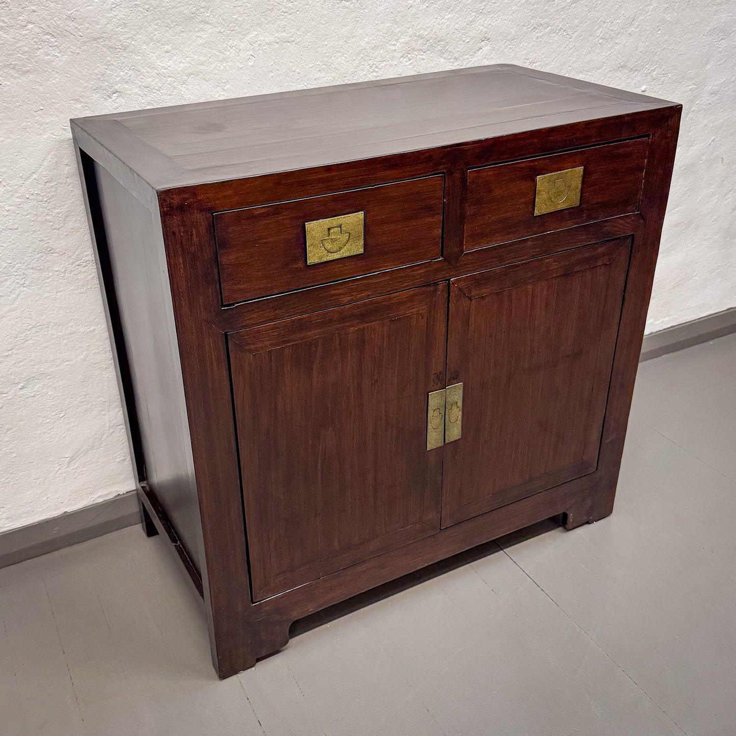 Wooden cabinet with brass handles on a light gray floor and wall.