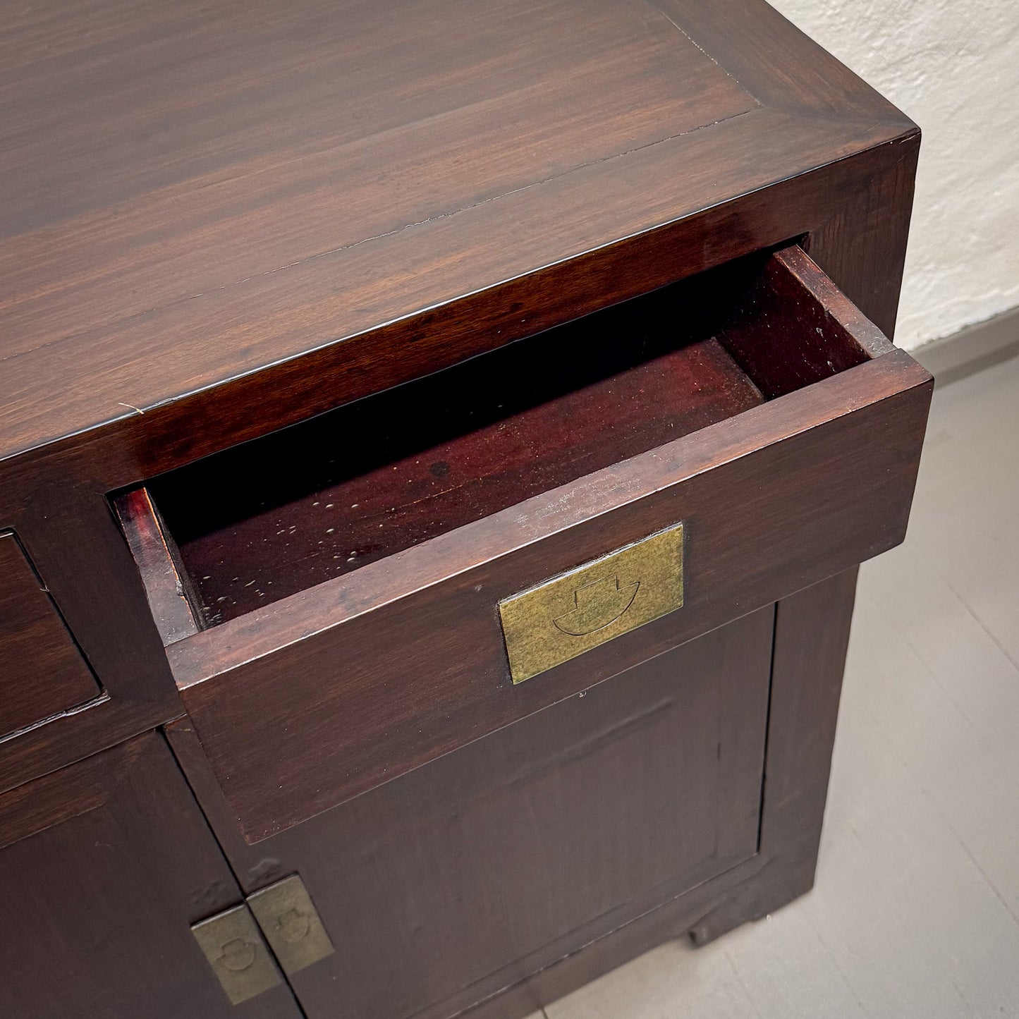 Wooden cabinet with an open drawer and brass hardware on a light background
